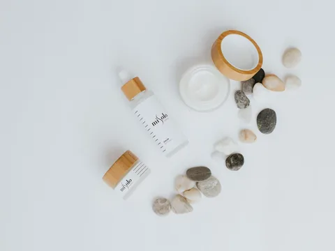 Overhead flat lay of skincare jars and pebbles arranged on a pale surface.