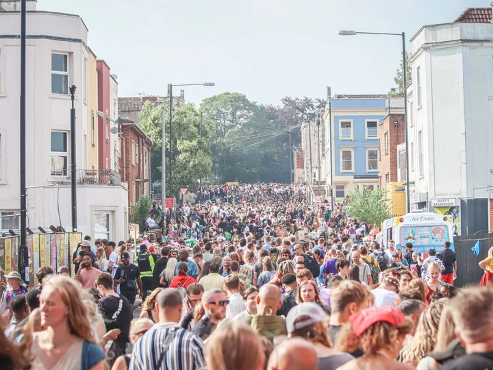 A packed British street filled with people between rows of terraced houses.