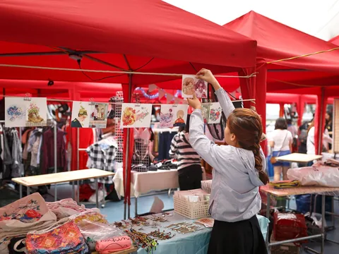 A shopper reaching across a red canopy stall to take something off the display.