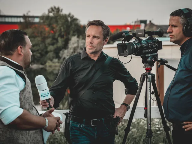 A camera and a handheld microphone set up to record someone speaking outdoors.